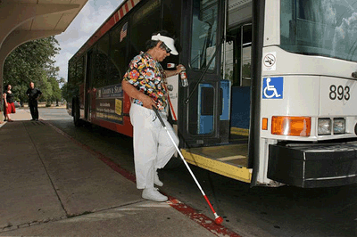Picture of older woman using white cane, getting on bus