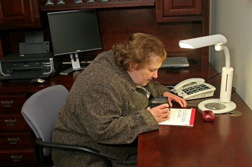Older woman reading at desk with light and magnifier