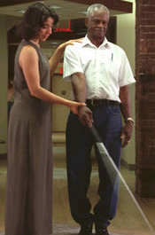 A woman demonstrating proper white cane use to an older man