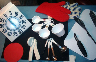A selection of adapted kitcen items, including oven mitts, a bold print timer, and adapted measuring cups and spoons