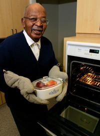 an older man proudly holding a casserole dish by the oven