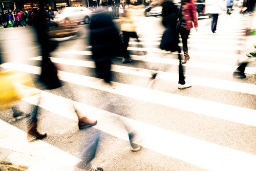People cross a busy city street. Image is blurred.