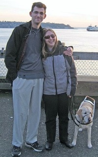 Alena and her husband Steve, posing by the water with guide dog Midge