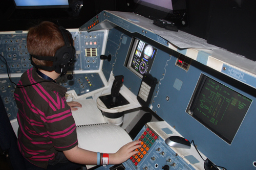 child at the controls of a space shuttle Endeavor mockup, with braille manual on his lap