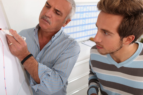 Older man and younger man looking at graph on whiteboard. 