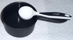 A white measuring spoon placed over the handle of a dark measuring cup for better contrast