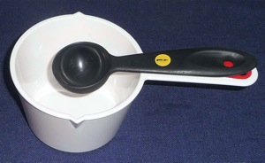 A dark measuring spoon placed over the handle of a white measuring cup for better contrast