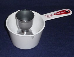 A silver jigger placed inside a white one-cup flat-bottomed measuring cup