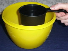 A dark measuring cup placed over the rim of a larger bright yellow bowl