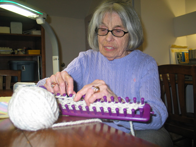 Chralotte Schrier working on a handheld loom under a task light