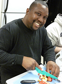 Dennis smiles as he practices chopping vegetables in the men's only cooking class offered by Second Sense