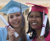 two young women in graduation caps and gowns, holding degrees