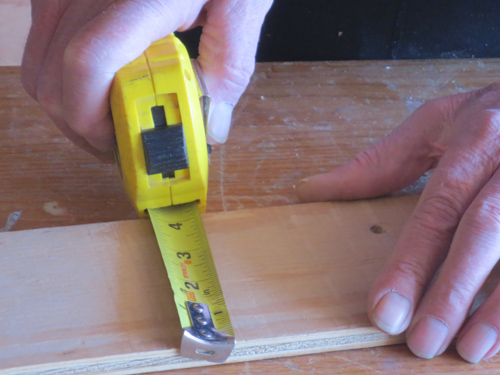 closeup of hands holding a locking tape measure in place on a board