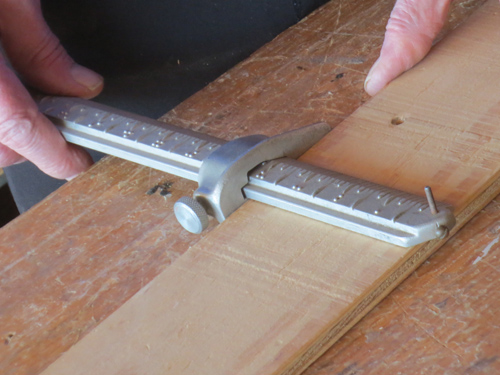 A person's hands holding a one-foot ruler with tactile and braille markings against a board