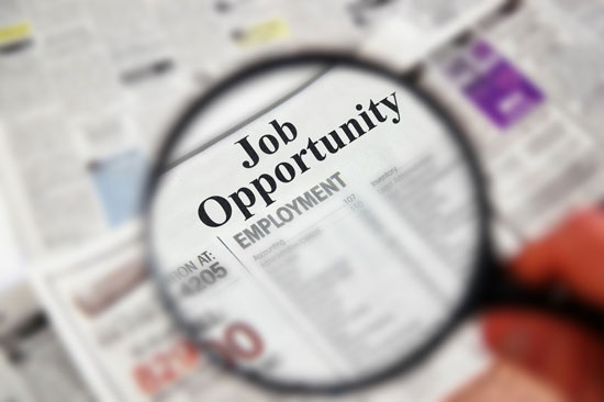 Magnifying glass over newspaper classified section with 'Job Opportunity' text