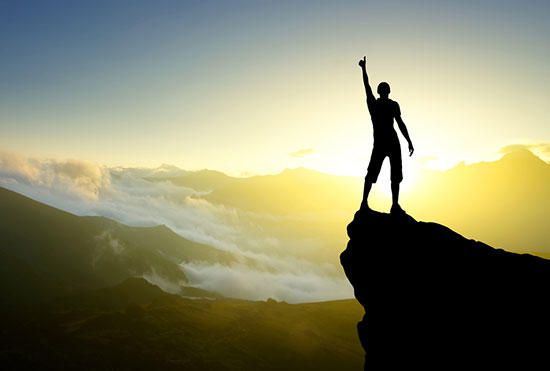 Silhouette of a mountain climber, at the summit, giving a thumbs-up.