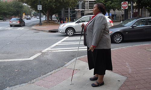 Empish standing at a street corner, white cane in hand