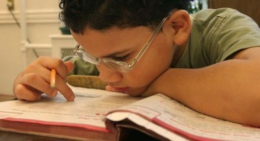 student wearing glasses leans in close to his schoolbook