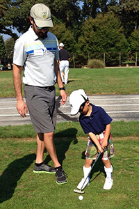 a volunteer coaches a young boy who is visually impaired and learning to play golf