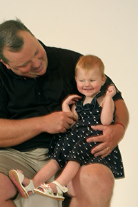dad smiling at his young visually impaired daughter, who is sitting on his knee, smiling
