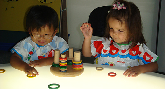   Two visually impaired preschoolers play with brightly colored stacking rings on a light table. Photo courtesy of Anchor Center for Blind Children, Denver, CO