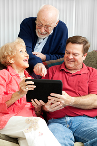 a man seated on a couch, showing an iPad to a senior couple