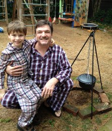 Kevin and his son in their pajamas next to a campfire after a night of camping out.