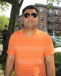 Syed Hassan standing outside wearing an orange and white striped shirt; a city street in the background