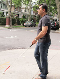 Syed using his white cane to navigate down a sidewalk in the city