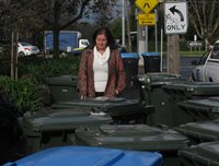 A blind pedestrian navigates through a sidewalk full of trash bins