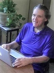 Maxwell wearing a purple shirt and smiling at the camera