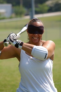 Dee blindfolded holding up a bat and wearing a white tank top