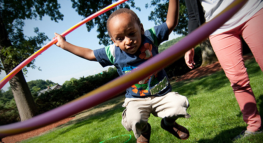 a young boy jumping, holding a hula hoop around himself