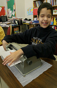 smiling boy using braillewriter in the classroom
