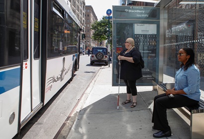 Two women with white canes wait for a NYC transit bus