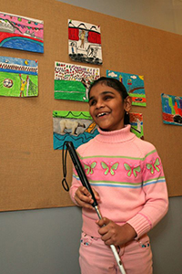 girl with white cane standing by a colorful school bulletin board