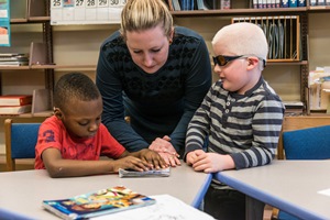 A teacher works with two children with visual impairments in a     classroom