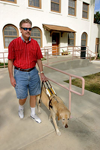 man walking with dog guide along a building's exit ramp