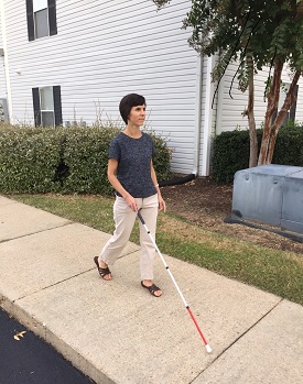 Kendra using white cane on sidewalk