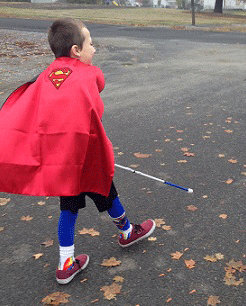 Eddie dressed as Superman, walking with his white cane