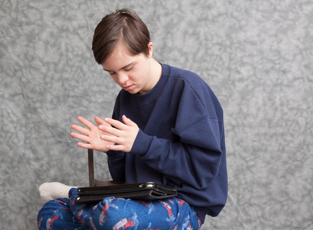 Image of a boy sitting with legs crossed, an iPad on his lap. His hands are clapping in the air.