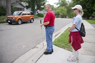 individual crossing street using cane with instructor observing