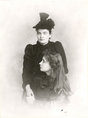 Helen Keller and Anne Sullivan Macy formal portrait. Keller is seated in front of Macy. With her left hand, Keller holds her teacher's right hand, circa 1893