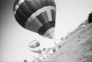 Two hot air balloons in a field surrounded by several spectators.