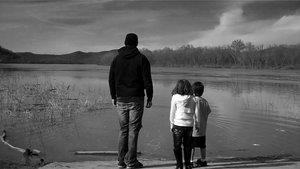 A father with young son and daughter standing on the bank of the Ohio River looking out across the water. Hills and trees line the other side of the river