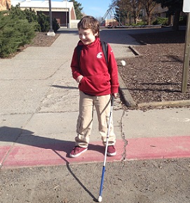 Eddie with white cane standing outside his school