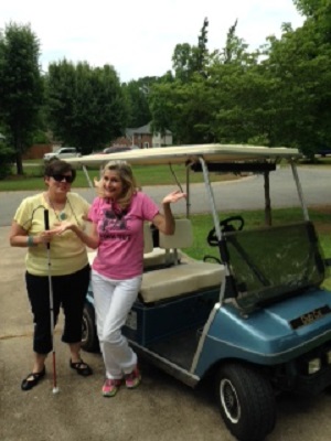 two women, one with cane, standing by golf cart