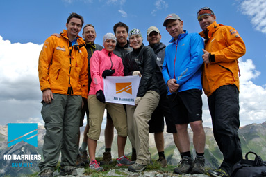 Group of men and women posing on a mountain summit with the No Barrier sign