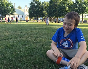 Eddie sitting on grass at park by a softball game