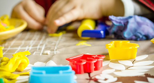 closeup of child's hands playing with colorful dough and plastic molds